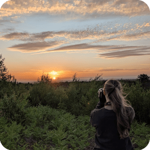 a woman taking a photo of a sunset over trees