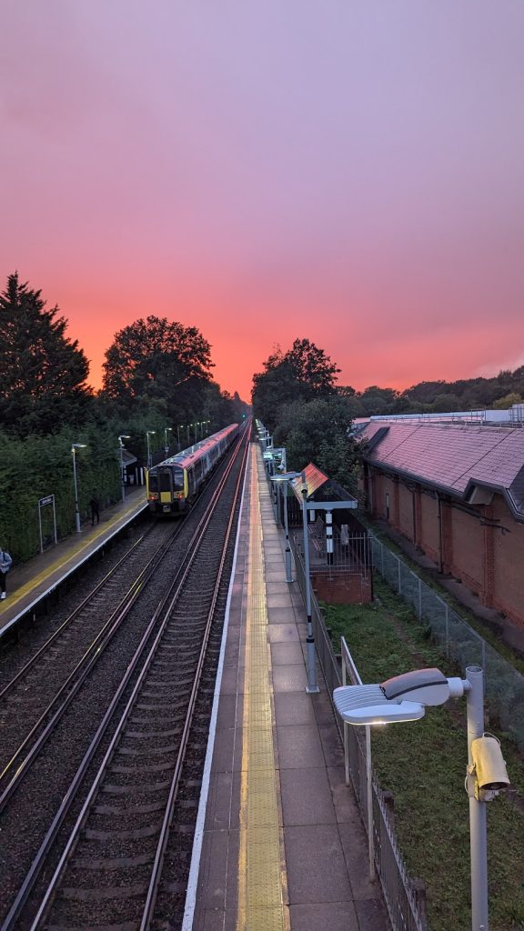 a train stop with a pink and purple sunset behind it