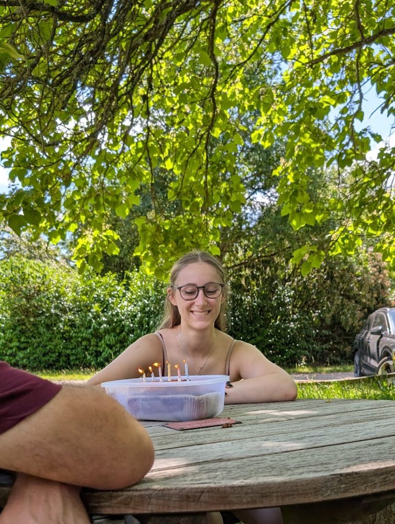 a girl smiling at a birthday cake in a Tupperware box. It has candles on it