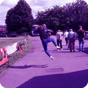 a family walking while a girl does a silly jump in a car park